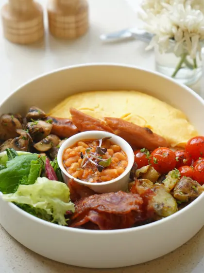 Our breakfast bowl is a complete meal, featuring a classic omelette, sausages, bacon, sautéed mushrooms, baked beans, and fresh greens. It’s the perfect fuel for a busy day.