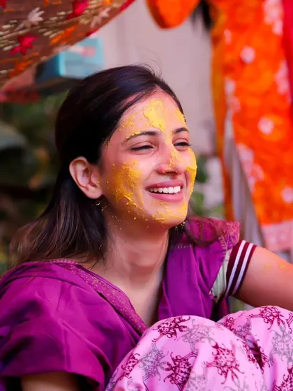 A bright and colourful shot of the bride smiling as turmeric is applied to her face. The traditional phulkari dupatta adds a beautiful cultural element to the photo.
