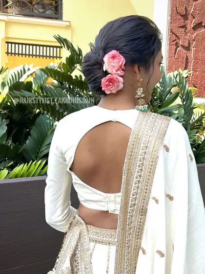 A simple and elegant low bun adorned with two fresh pink roses. This is a classic choice for any wedding guest or for a simple engagement ceremony.