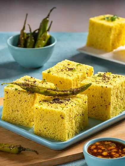 Soft and spongy Khaman Dhokla, a savory steamed cake from Gujarat, garnished with fried green chilies.