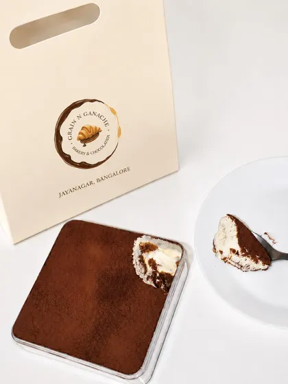 Tiramisu is ready in our takeaway box, with cocoa on top and a spoonful showing the coffee-soaked layers.