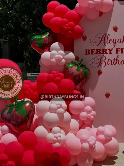 A close-up of a "Berry First Birthday" balloon arrangement, featuring shades of pink and red with strawberry-shaped foil balloons.