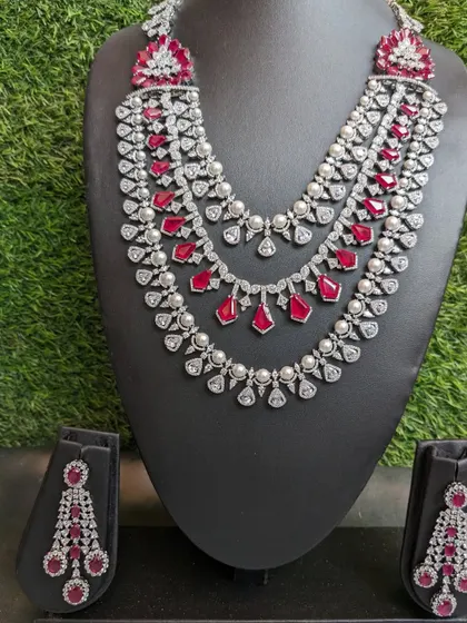 This exquisite three-layered necklace with ruby, pearl, and AD stones is perfect for a red carpet look or a grand reception. The matching earrings complete this glamorous and sophisticated ensemble.