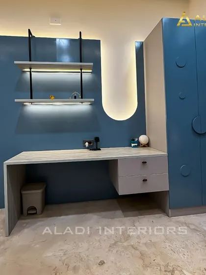 A functional and stylish study area within a bedroom, featuring a modern desk and backlit wall shelves. The adjacent blue wardrobe has unique circular handles.