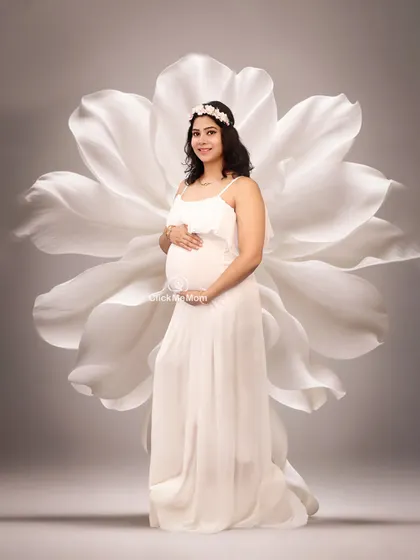 A portrait of blossoming motherhood. Here, the mom-to-be stands before a large, beautifully crafted white flower prop, creating a simple yet striking and artistic image.