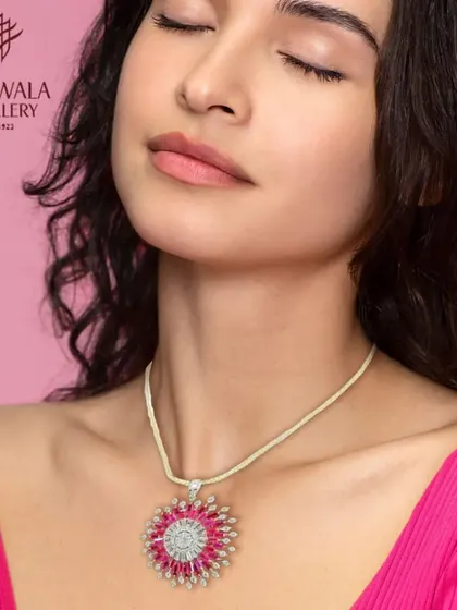 A stunning pendant necklace featuring a large ruby-colored stone in a sunburst diamond setting. This piece is designed to be a bold and glamorous focal point.