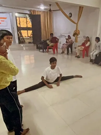 A young student demonstrates a perfect split in the middle of the training hall. His fellow students watch, learning and getting motivated by his dedication.