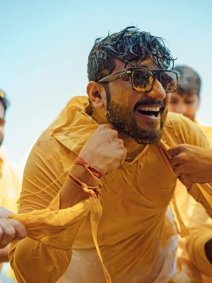 The groom's friends playfully tear his shirt during a fun-filled Haldi ceremony, a moment of pure candid laughter.