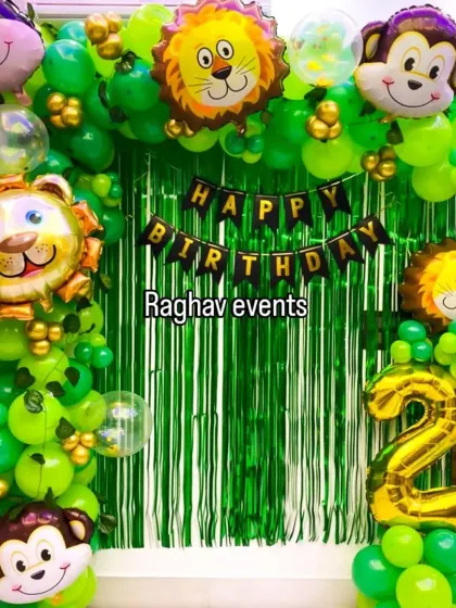 A fun jungle-themed birthday decoration. This setup includes a green foil curtain backdrop, a green balloon arch, and large foil balloons of jungle animals like lions and monkeys.