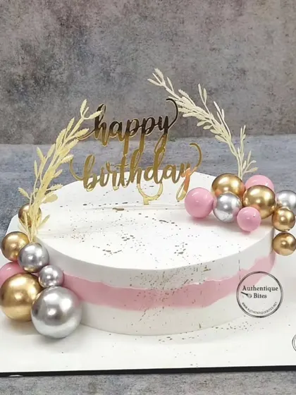 A simple and chic birthday cake. The pink and white base is adorned with a garland of pink, gold, and silver spheres.