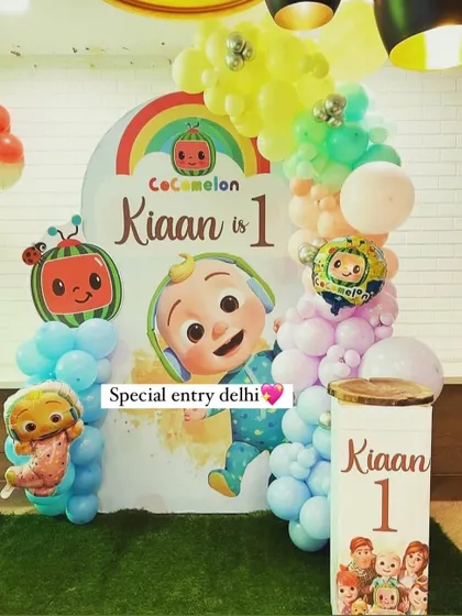 A Cocomelon themed backdrop for Kiaan's first birthday. The setup includes an arched backdrop, a pastel balloon garland, and a custom pedestal with the child's name and age.