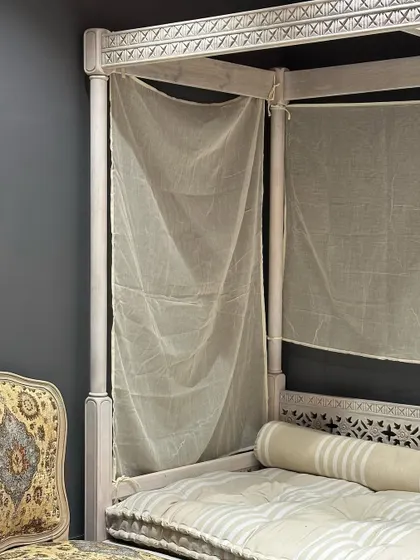 A detail shot of a custom-made poster daybed with intricate carving details. This piece combines traditional craftsmanship with a distressed white finish for a vintage-inspired look.
