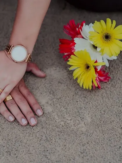 A detail shot of the couple's hands resting on the sand next to a small bouquet of colorful flowers, symbolizing the simple, beautiful moments of their love story.