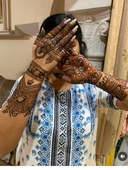 A bride showing off her mehandi, which features traditional symbols and patterns extending up her arms.