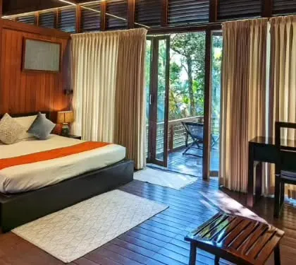The interior of an elegant nature lodge in Coorg, featuring warm wooden tones and a private balcony. It's the perfect cozy retreat after a day of exploring the coffee plantations.