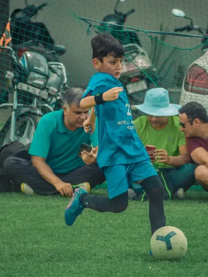 A young player dribbles while parents watch from the sidelines.