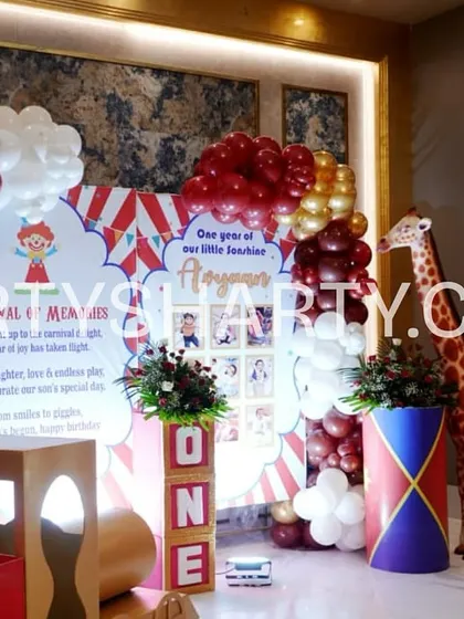 A photo corner at a carnival party, featuring a personalized backdrop, balloon columns, and a friendly giraffe prop for fun pictures.