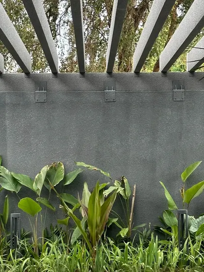 A detail of the exterior landscaping, where lush greenery is planted against a textured concrete wall. The overhead pergola and subtle uplighting highlight the integration of natural and built elements.