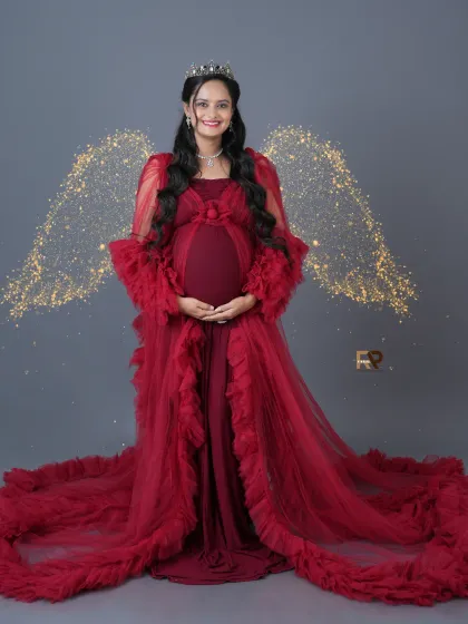 Feel like a celestial queen. This portrait combines a regal crown, a flowing red gown, and sparkling angel wings for the ultimate fantasy maternity shoot.