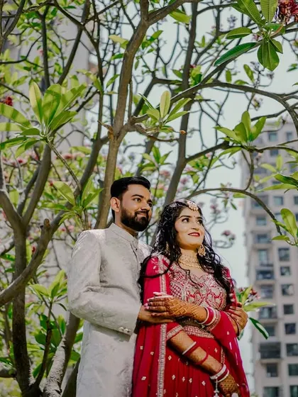 A wide-angle shot of the couple standing under a tree, with modern buildings in the background. This portrait beautifully blends nature with an urban landscape, reflecting a modern love story.