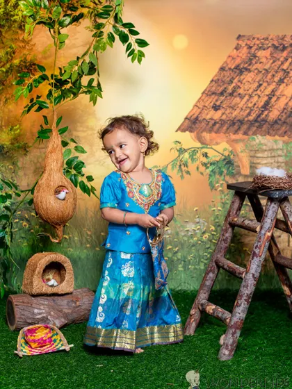 A toddler in a beautiful blue traditional outfit, smiling sweetly in a village-themed setting with a weaver bird nest prop. It’s these little details that make a themed shoot special.