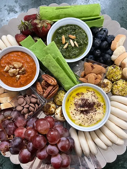 A vibrant grazing board perfect for intimate gatherings. It features a trio of my signature dips: classic hummus, spicy muhammara, and fresh pesto, served with a variety of crackers, breads, fruits, and nuts.