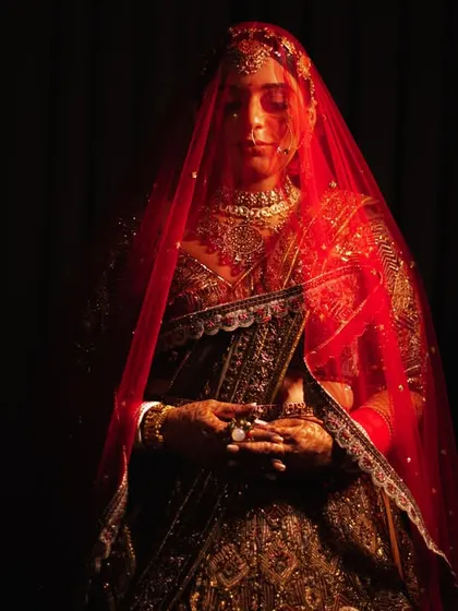 A full-length portrait of the bride under her red veil, shrouded in shadow. A very dramatic and artistic bridal shot.