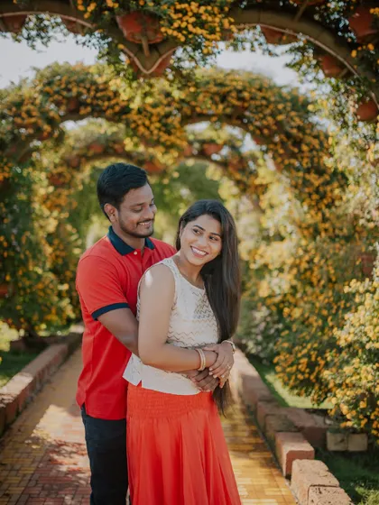 A bright and happy portrait of a couple framed by an arch of yellow flowers.