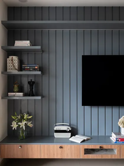This TV unit features a grey paneled wall and a two-tone console in grey and light wood, offering a mix of open and closed storage.