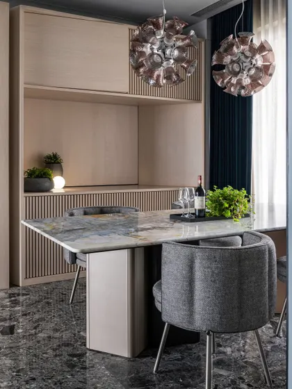 A closer look at the dining table, showing the contrast between the marble top, grey upholstered chairs, and statement lighting.