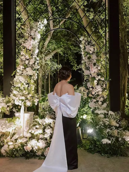 A guest stands before a magnificent floral arch, a perfect photo opportunity at this Chanel-inspired bachelorette dinner. The arch, overflowing with white blossoms, exemplifies how we create interactive and visually stunning moments within an event.