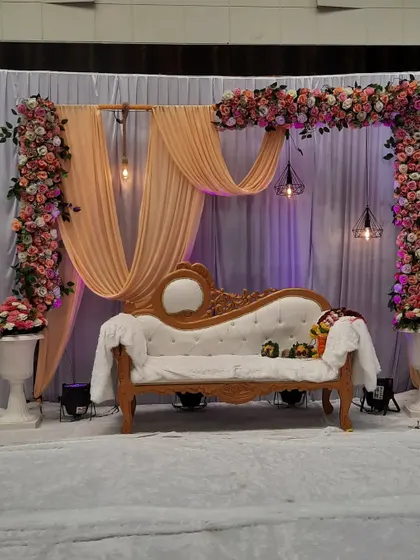 A still shot of a lovely engagement stage with peach drapes and a floral frame. The hanging industrial-style lamps add a modern touch to the romantic setup.