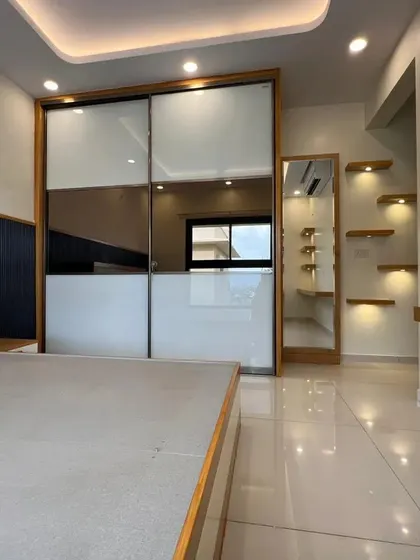 A bedroom featuring a large sliding wardrobe with mirrored and white panels, which helps to make the space feel larger and brighter. The design also includes a built-in dressing area with illuminated shelves.