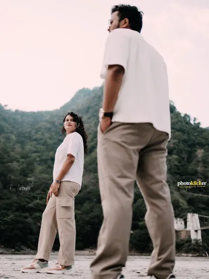 A creative portrait of a couple on a riverbank, with the man in the foreground and the woman in the background, creating a sense of depth.