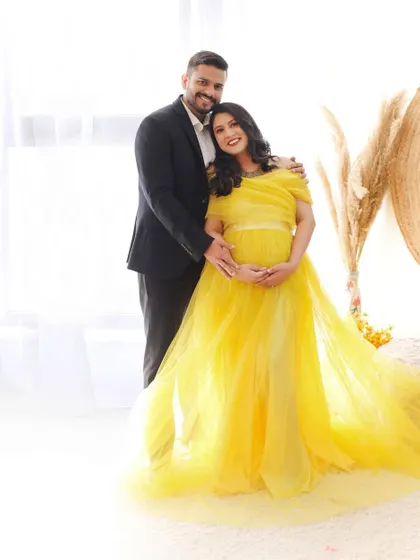 A full-length portrait of a couple, with the mom-to-be wearing a flowing yellow gown. The bright, high-key lighting creates a dreamy and ethereal feel.