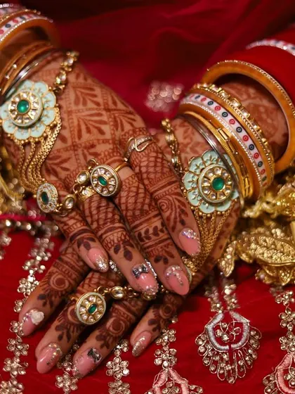 A detailed shot of a bride's hands, adorned with intricate henna, rings, and traditional red and white bangles.