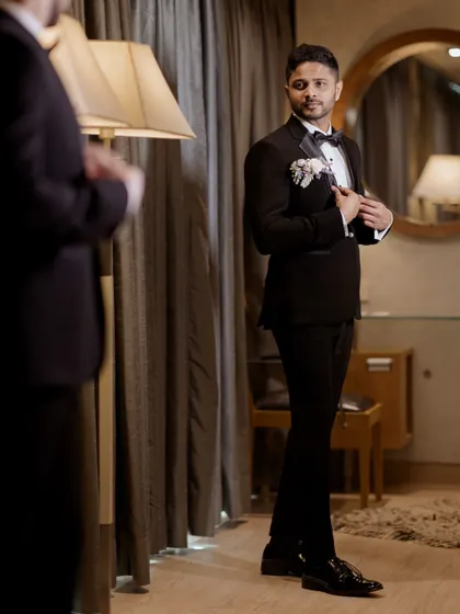 The groom adjusts his tuxedo while looking in the mirror, a moment of final preparation.