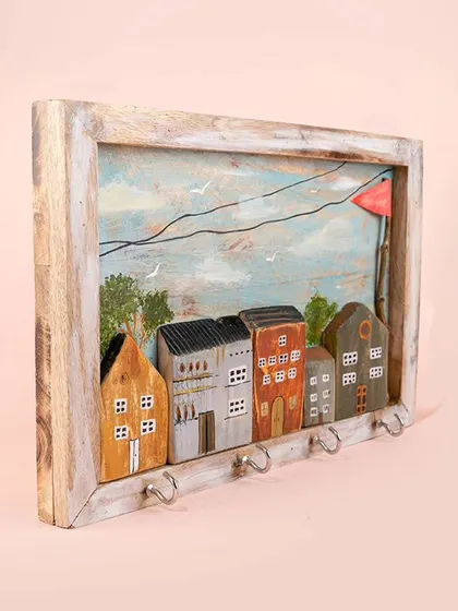 An angled view of the miniature house keyholder, showing its 3D construction. The wooden houses are set against a painted sky, creating a beautiful little diorama.