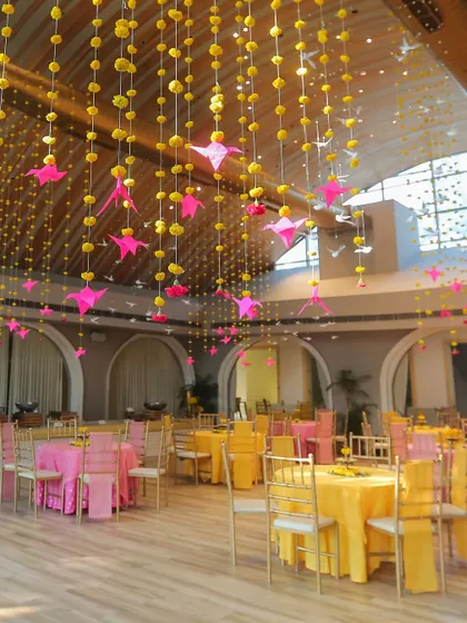 The high ceiling of our indoor hall adorned with hanging strings of yellow flowers and pink origami birds, creating a whimsical atmosphere.