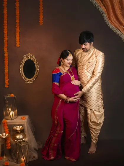 A tender moment where the couple cradles the baby bump together. The marigold garlands and warm lighting create a festive and sacred atmosphere.