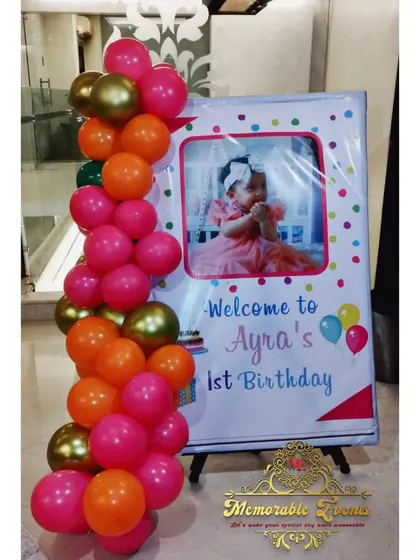 A welcome sign for a first birthday, framed with a colorful balloon garland.