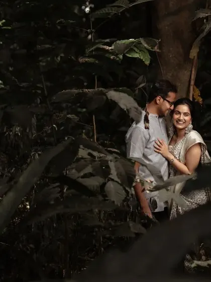 A romantic pre-wedding portrait in a dark, moody forest setting. The lighting and composition create a very intimate and artistic feel.