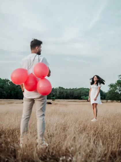 A beautiful, candid shot of a groom holding balloons, with his bride-to-be in the background, her hair blowing in the wind.