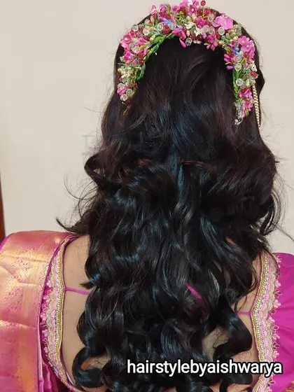 A beautiful curly hairstyle for a festive event. The hair is styled in a half-updo with a stunning fresh flower hairpiece, and the rest of the hair is in voluminous curls.
