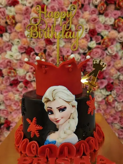 A close-up of the 'Frozen' themed cake, showing the details of the red fondant crown and the character print of Elsa.