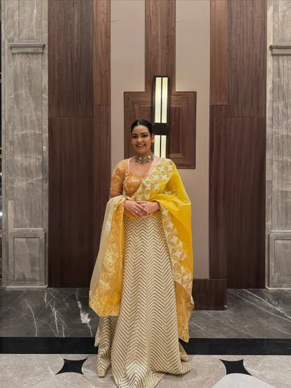 Dressed for a wedding in a beautiful yellow and off-white lehenga. The chevron-patterned skirt and intricately embroidered blouse create a look that is both traditional and contemporary.