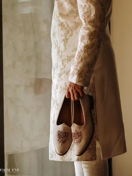A detail shot focusing on the groom's hands holding his intricately embroidered mojari shoes, a small but significant part of his wedding attire.