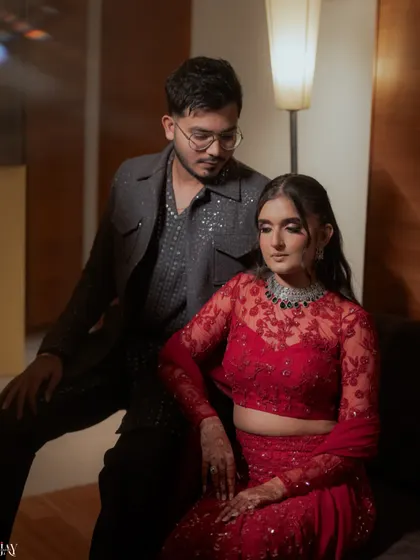 A stylish indoor portrait of the couple, showcasing their coordinated red and grey outfits for the Sangeet.