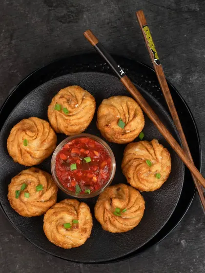 A top-down shot of beautifully pleated fried momos with a spicy dipping sauce. The dark, moody styling makes the golden-brown momos stand out, creating a dramatic and appealing image.