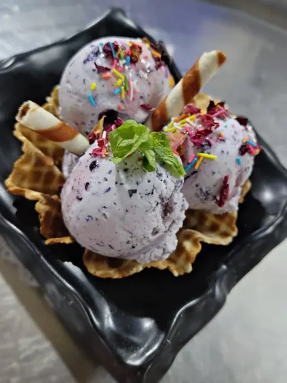 Our seasonal Fresh Jamun Ice Cream. Made with real jamun fruit, this ice cream has a beautiful color and a unique sweet and tart flavor, served in a waffle cone bowl.